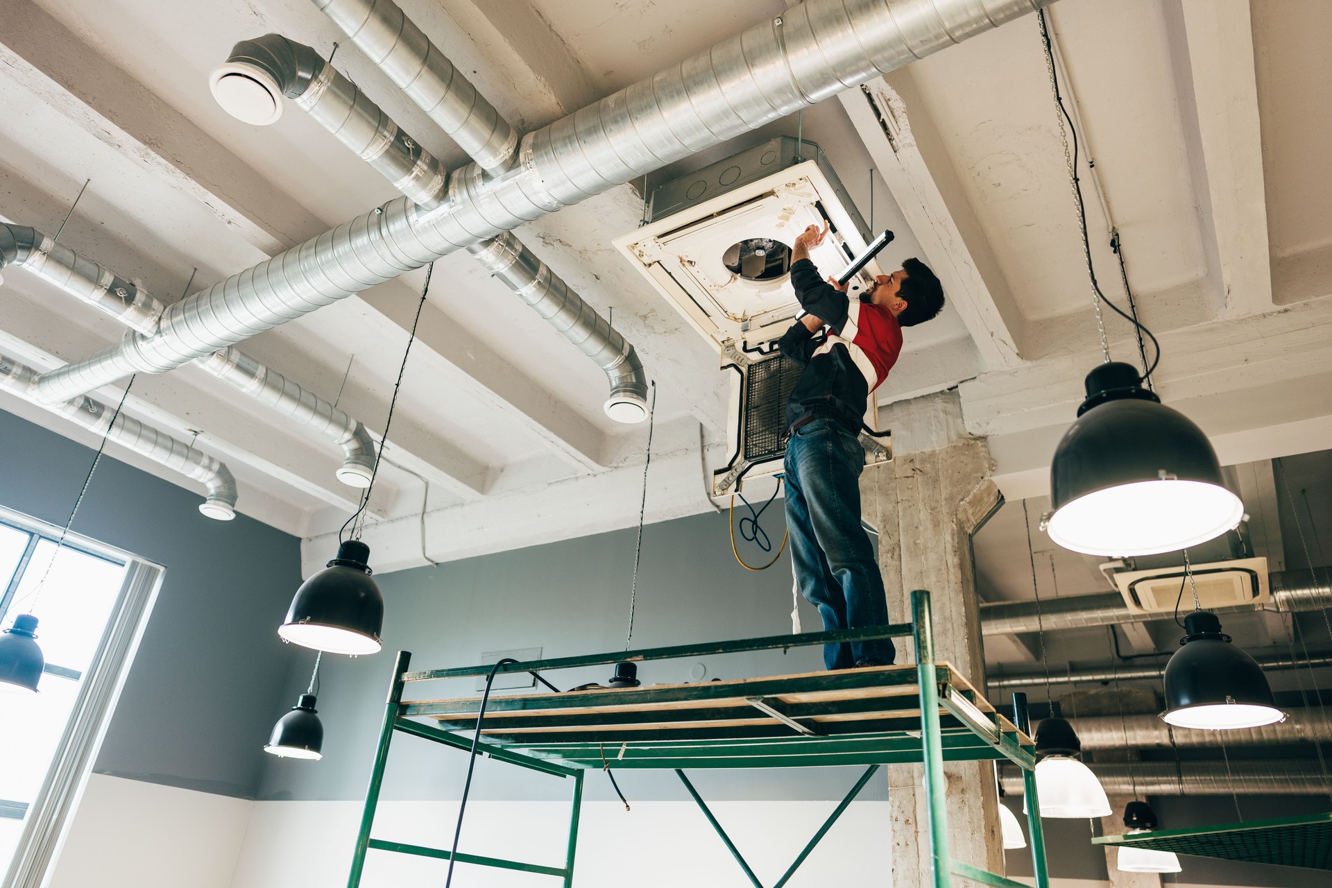 Worker repairing air conditioning unit in modern commercial building during daylight hours