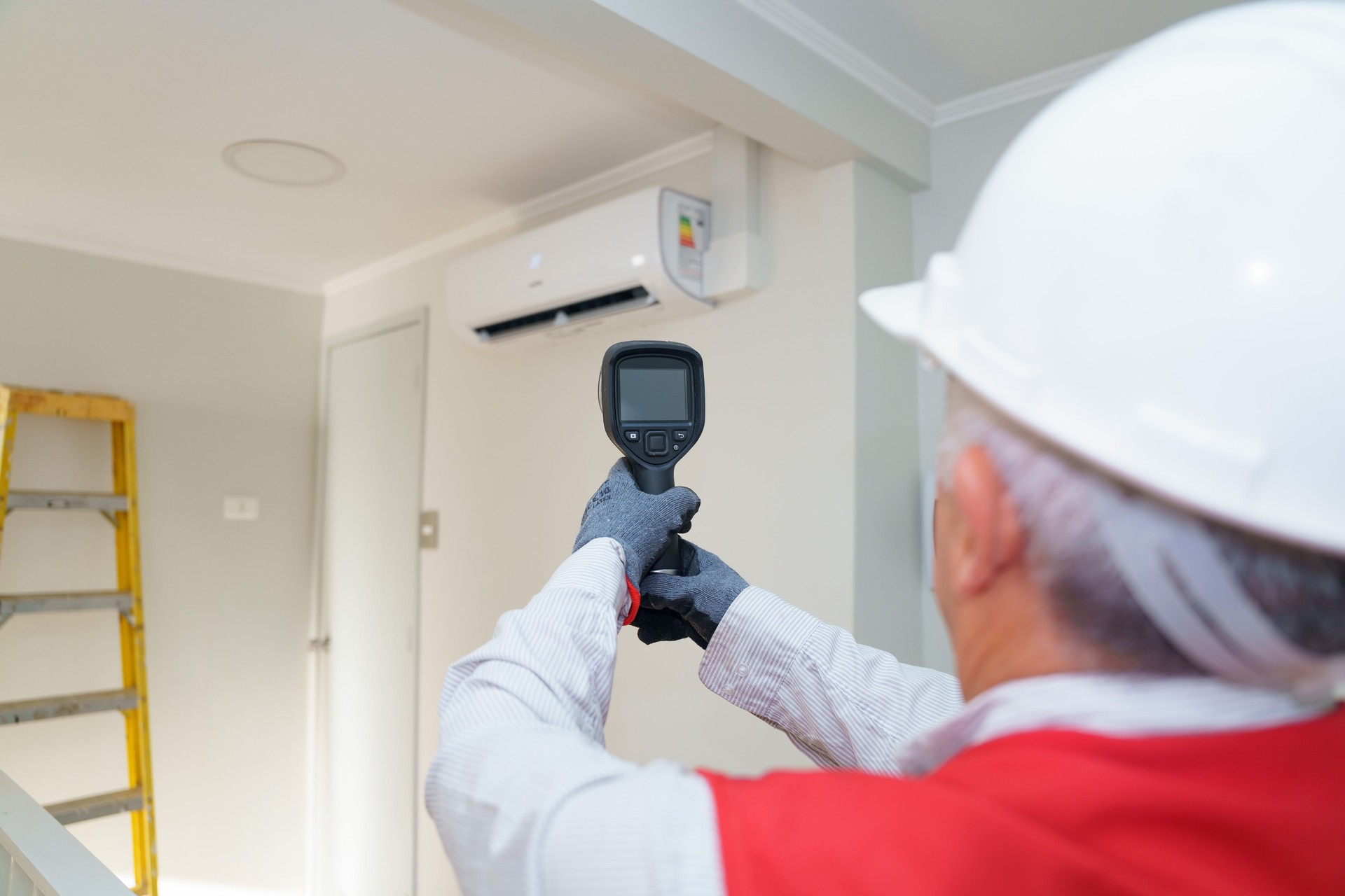 Latin american senior technician checking air conditioning using thermal imager